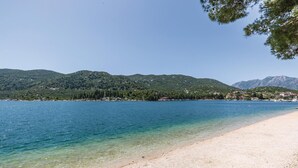Una spiaggia con acque limpide, una riva sabbiosa e sullo sfondo colline e montagne verdi.