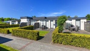 Een modern gebouw met een verhard pad, verzorgde hagen en buiten zitgedeeltes.
