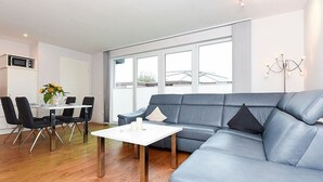 Een moderne woonkamer met een grijze leren bank, een witte salontafel en een eetgedeelte met een witte tafel en zwarte stoelen.