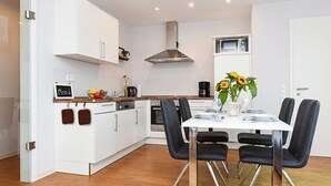 Een moderne keuken met witte kasten, een roestvrijstalen afzuigkap en een eethoek met een witte tafel en zwarte stoelen.