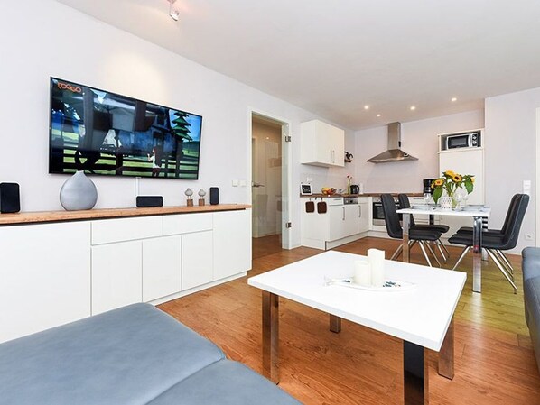 A modern living room with a flat-screen TV, a white coffee table, and a grey sofa.