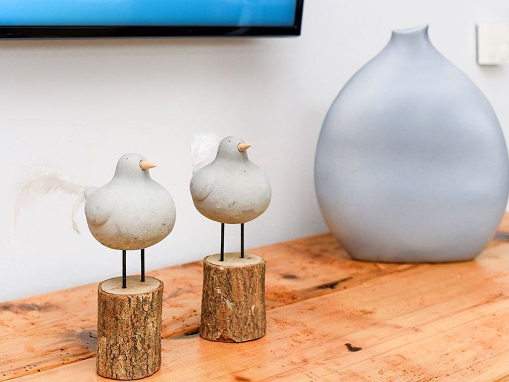 Twee vogelbeeldjes op houten voetstukken, een grijze vaas en een televisie aan een muur.