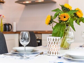 A dining table set with plates, cutlery, and a glass of water. A vase with yellow flowers and a decorative candle holder are also visible.