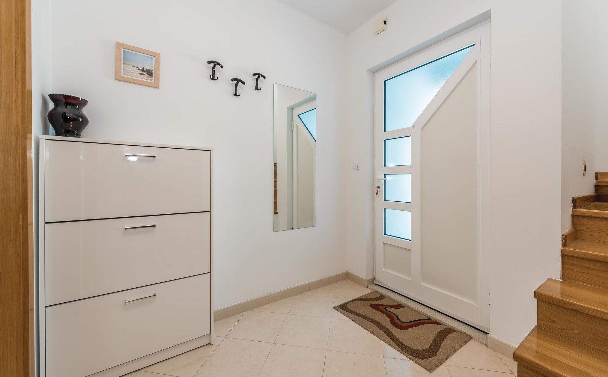Un pasillo con un armario blanco, un espejo y una puerta con paneles de vidrio esmerilado.