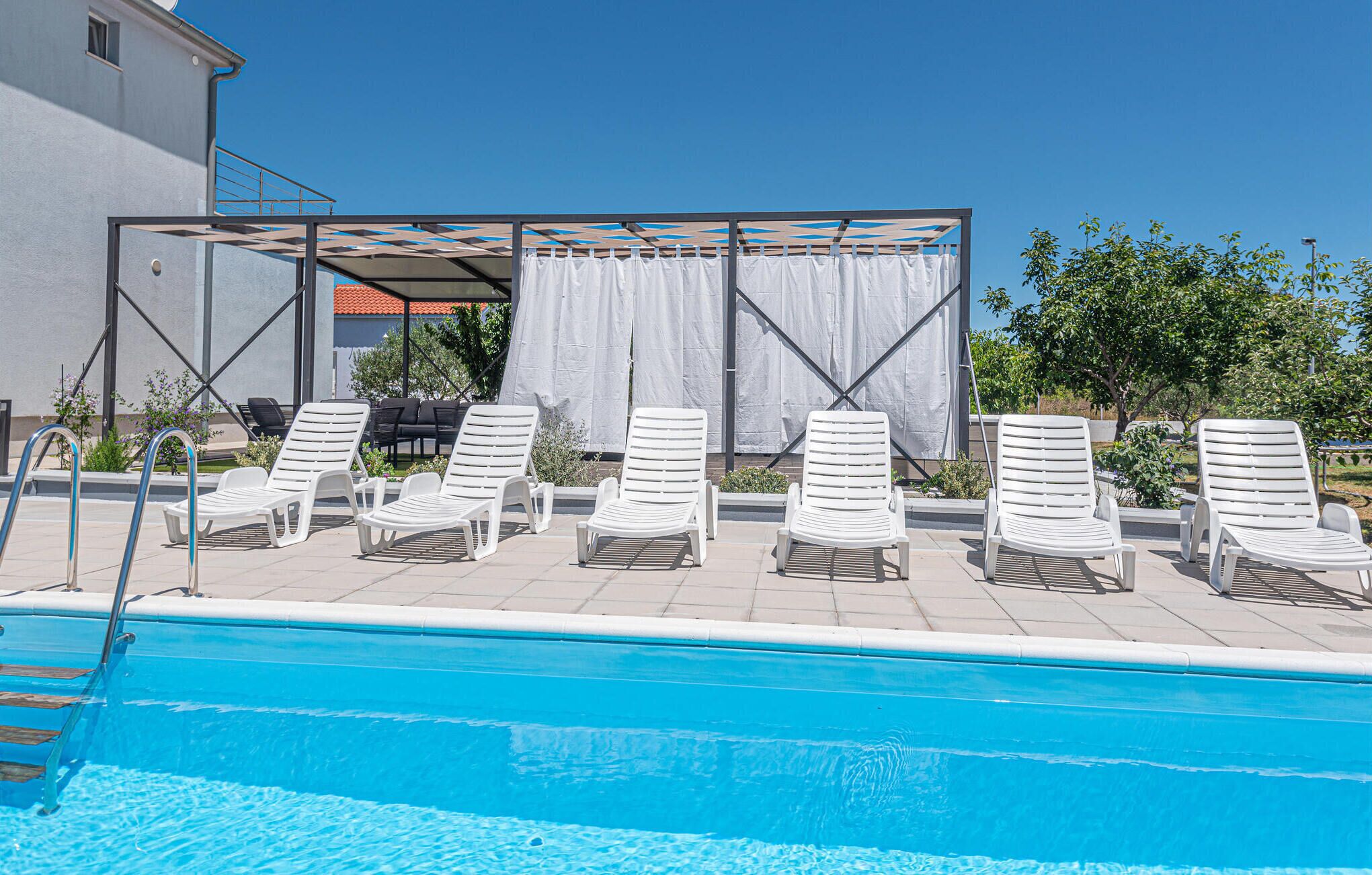 A poolside area with white lounge chairs and a covered seating area with white curtains.