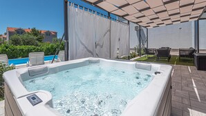 A hot tub with a control panel, surrounded by lounge chairs and a covered patio area.