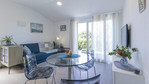 Een moderne woonkamer met een glazen eettafel, een blauwe bank en een aan de muur bevestigde televisie.