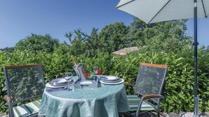 Een eettafel buiten, gedekt met een lichtgroene tafelkleed, met twee metalen stoelen met net rugleuningen en een witte parasol voor schaduw.