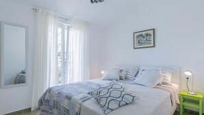 Een slaapkamer met een bed, een nachtkastje met een lamp, een lijst met een afbeelding aan de muur en een raam met gordijnen.