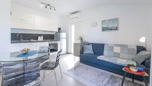 Een moderne keuken met witte kastjes, een glazen eettafel en een blauwe bank in de woonkamer.