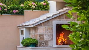 A stone-built outdoor fireplace with a fire burning inside, surrounded by a beige wall and a small window. - Villa Anima in Makarska, private pool (Makarska)