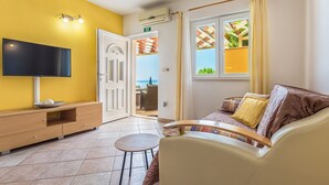 A living room with a TV, a sofa, a small table, and a door leading to a balcony. - Villa Anima in Makarska, private pool (Makarska)