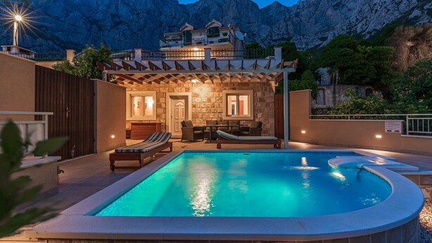 A swimming pool with lounge chairs, a stone wall, and a mountain backdrop. - Villa Anima in Makarska, private pool (Makarska)