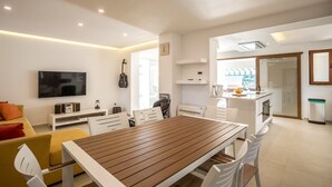 Una sala de estar moderna con una mesa de comedor de madera, sillas blancas, un sofá, un televisor y una guitarra.