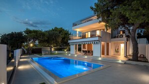Una casa moderna de dos pisos con piscina, mobiliario exterior y una zona de patio bien iluminada.