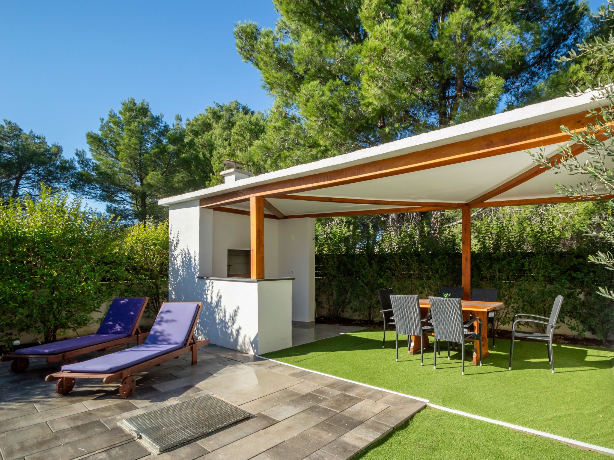 Un patio extérieur moderne agrémenté d’une pergola, de chaises longues, d’une table et de chaises.