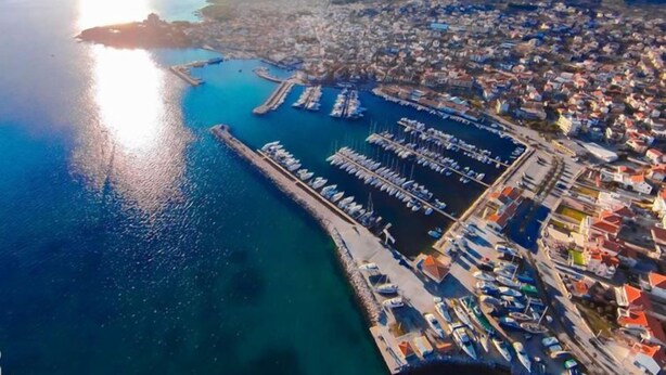 An aerial view of a coastal town with a marina, residential buildings, and a clear view of the surrounding landscape.