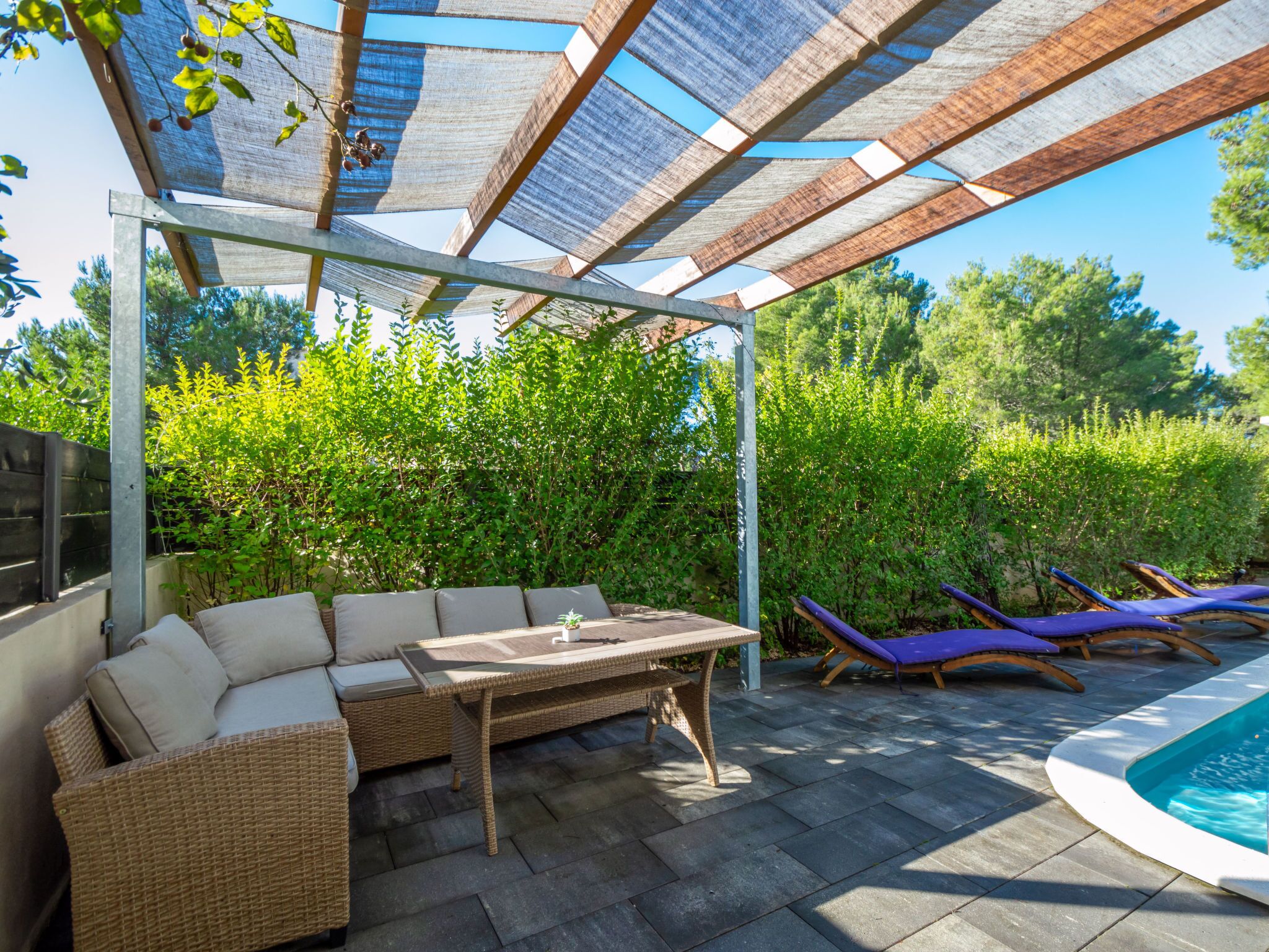Une terrasse extérieure dotée d’un espace salon abrité, d’une piscine et d’une végétation luxuriante.