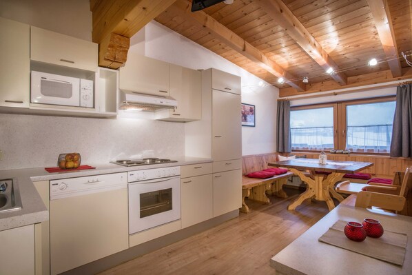 A kitchen with white cabinets, a microwave, a dishwasher, a stove, and a dining area with a wooden table and benches.