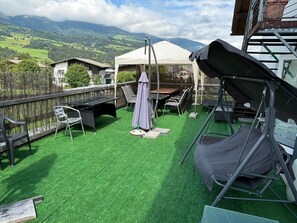 Enjoy panoramic views of the surrounding mountains from this rooftop terrace, featuring a table, chairs, swing set, and covered seating area.