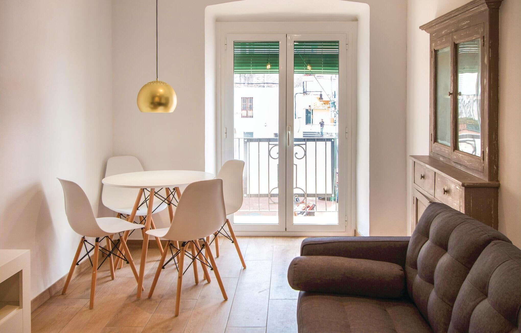 Een eetgedeelte met een ronde tafel en vier stoelen, een bank, een kast en een groot raam met een balkon.