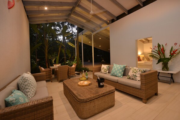 A modern outdoor living area with wicker furniture, a glass-enclosed patio, and tropical plants. - Pavilions in the Palms (Port Douglas)