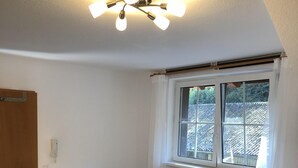 A small, well-lit room with a sofa, a small table, a radiator, and a window with curtains. - Neveu Josephsberg Winery (Durbach)