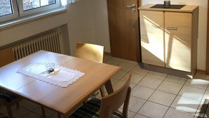 A dining area with a wooden table and chairs, a radiator, a window with curtains, a wooden cabinet, and a framed picture on the wall. - Neveu Josephsberg Winery (Durbach)