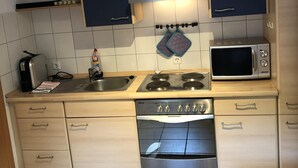 A compact kitchen with a gas stove, microwave, and oven. There are cabinets above the counter and a hanging pot rack. - Neveu Josephsberg Winery (Durbach)