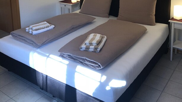 A neatly made bed with two pillows and two folded towels, a ceiling fan, and wall-mounted artwork. - Neveu Josephsberg Winery (Durbach)