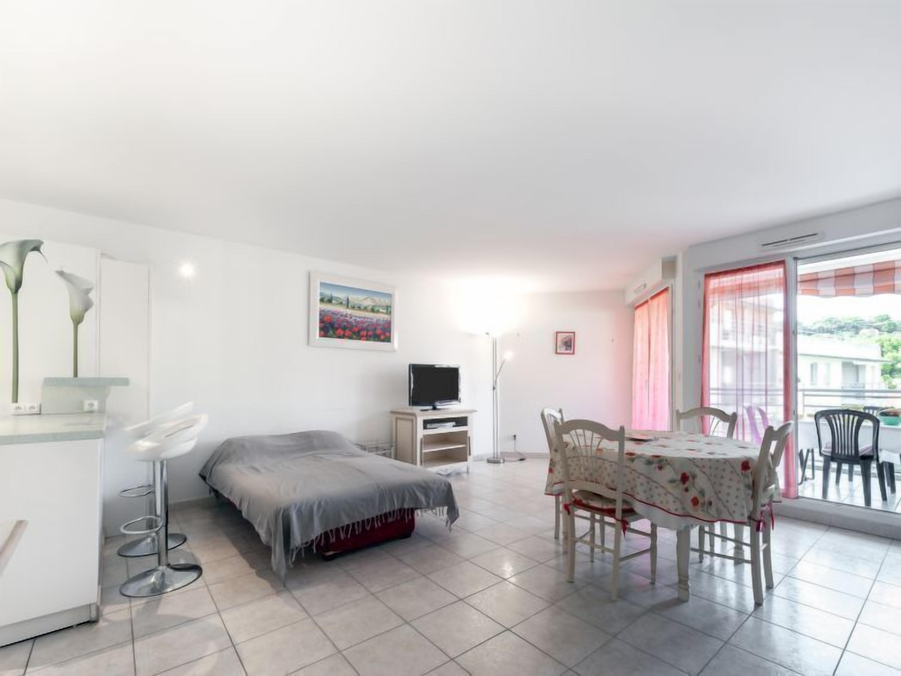 A modern bedroom with a bed, a TV, a desk, and a dining area with chairs.