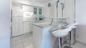 A modern kitchen with white cabinetry, a built-in oven, and a microwave. There is a small island with a sink and a bar stool. - Côté Port by Interhome (Cavalaire)
