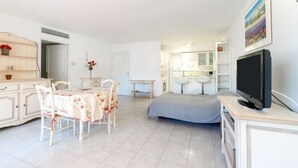 A bright living room with a dining table, chairs, a TV, and a kitchen area with a sink and bar stools. - Côté Port by Interhome (Cavalaire)