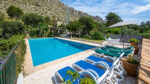 Una piscina con sillas de descanso, una terraza de madera y montañas al fondo.