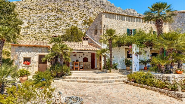 Un edificio de piedra con tejado de tejas, una escalera que lleva a una puerta y una montaña al fondo.