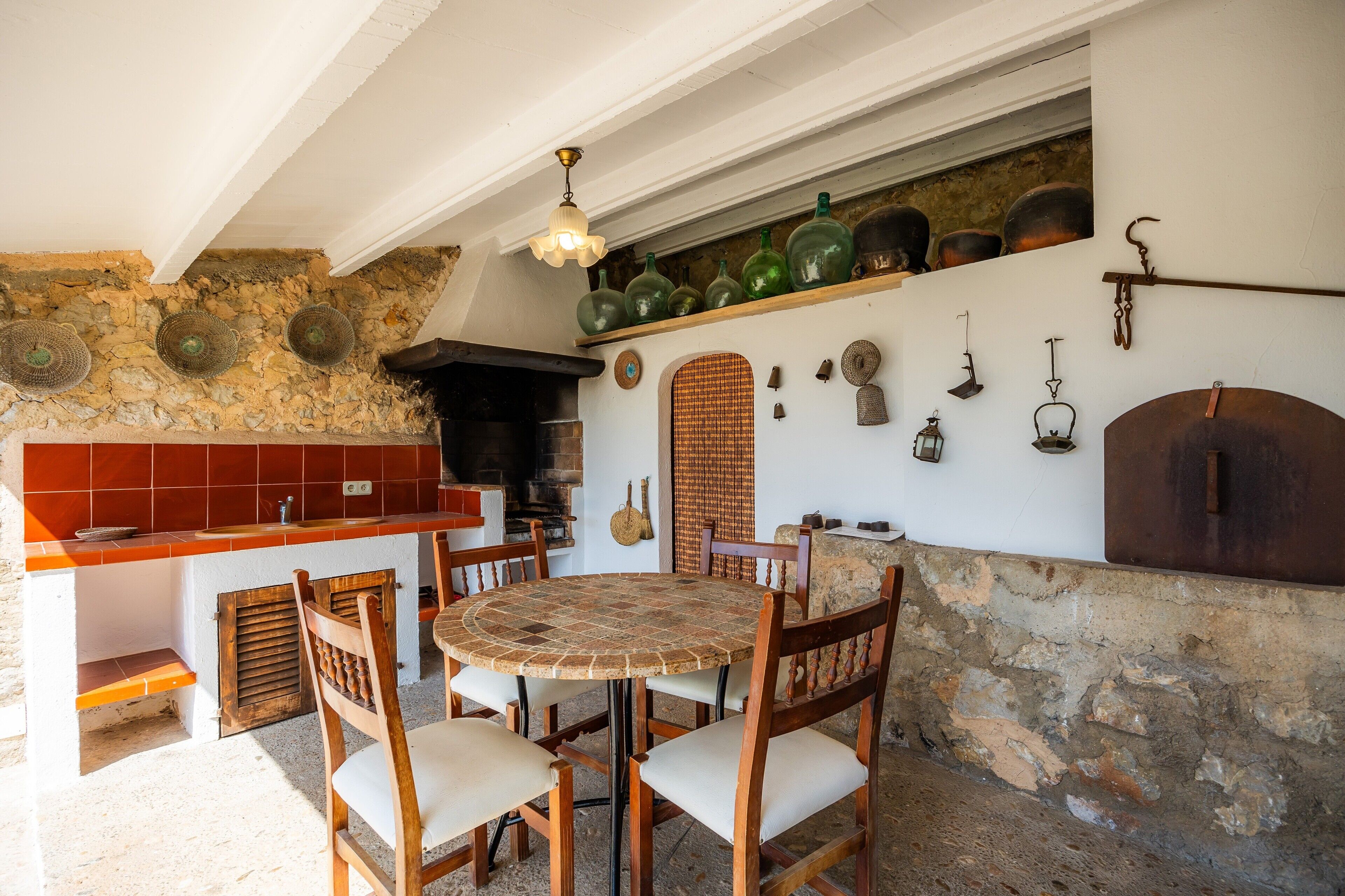 A rustic kitchen with a stone wall, wooden chairs, a round table, and various kitchen utensils.