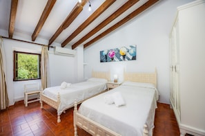 Une chambre avec deux lits, des poutres en bois, une fenêtre avec des rideaux, un climatiseur et un tableau au mur.