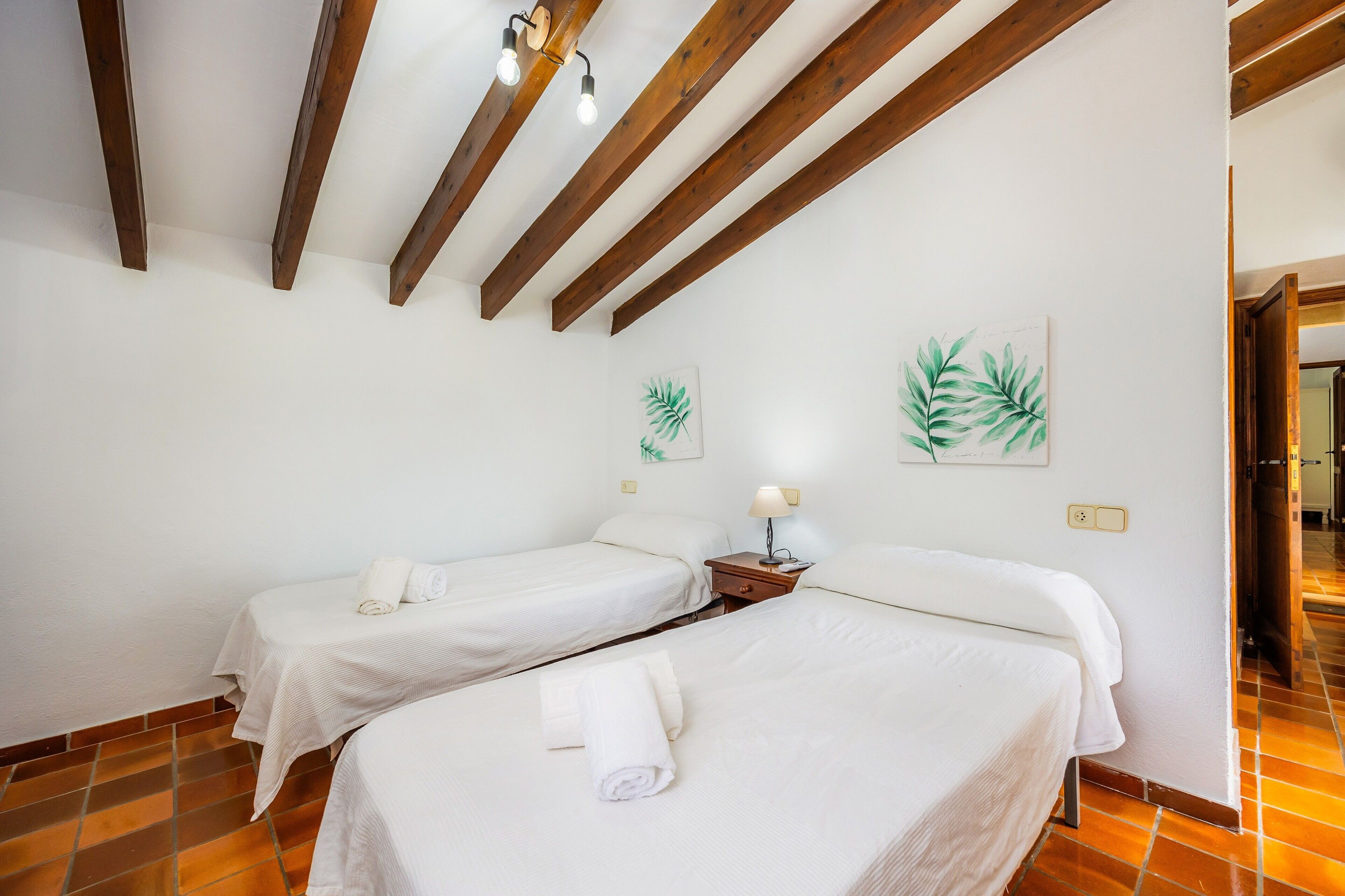 Een hotelkamer met twee bedden, houten balken in het plafond, een wandlamp en een schilderij van bladeren.