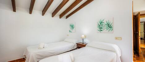Een hotelkamer met twee bedden, houten balken in het plafond, een wandlamp en een schilderij van bladeren.