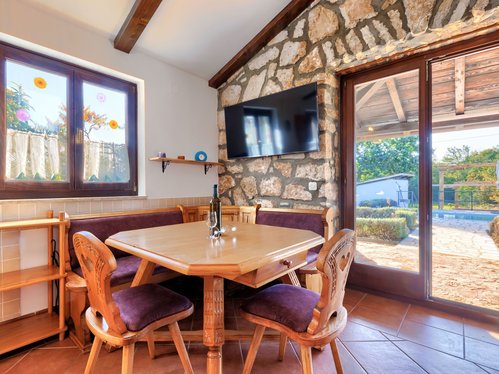Un comedor con pared de piedra, mesa de madera y sillas con cojines.