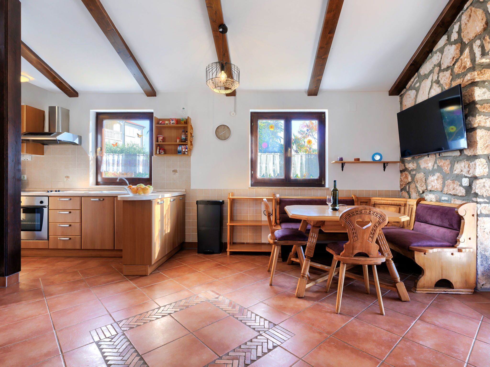 Een keuken met houten kastjes, een inbouwoven en een eethoek met een tafel en stoelen.