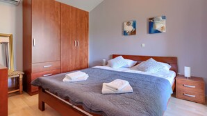 Ein Schlafzimmer mit einem großen Holzschrank, einem Bett mit grauer Steudecke und zwei abstrakten Bildern an der Wand.