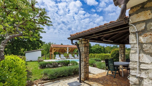 Eine Steinterrasse mit Pool, Sitzgelegenheiten im Freien und einer Pergola.
