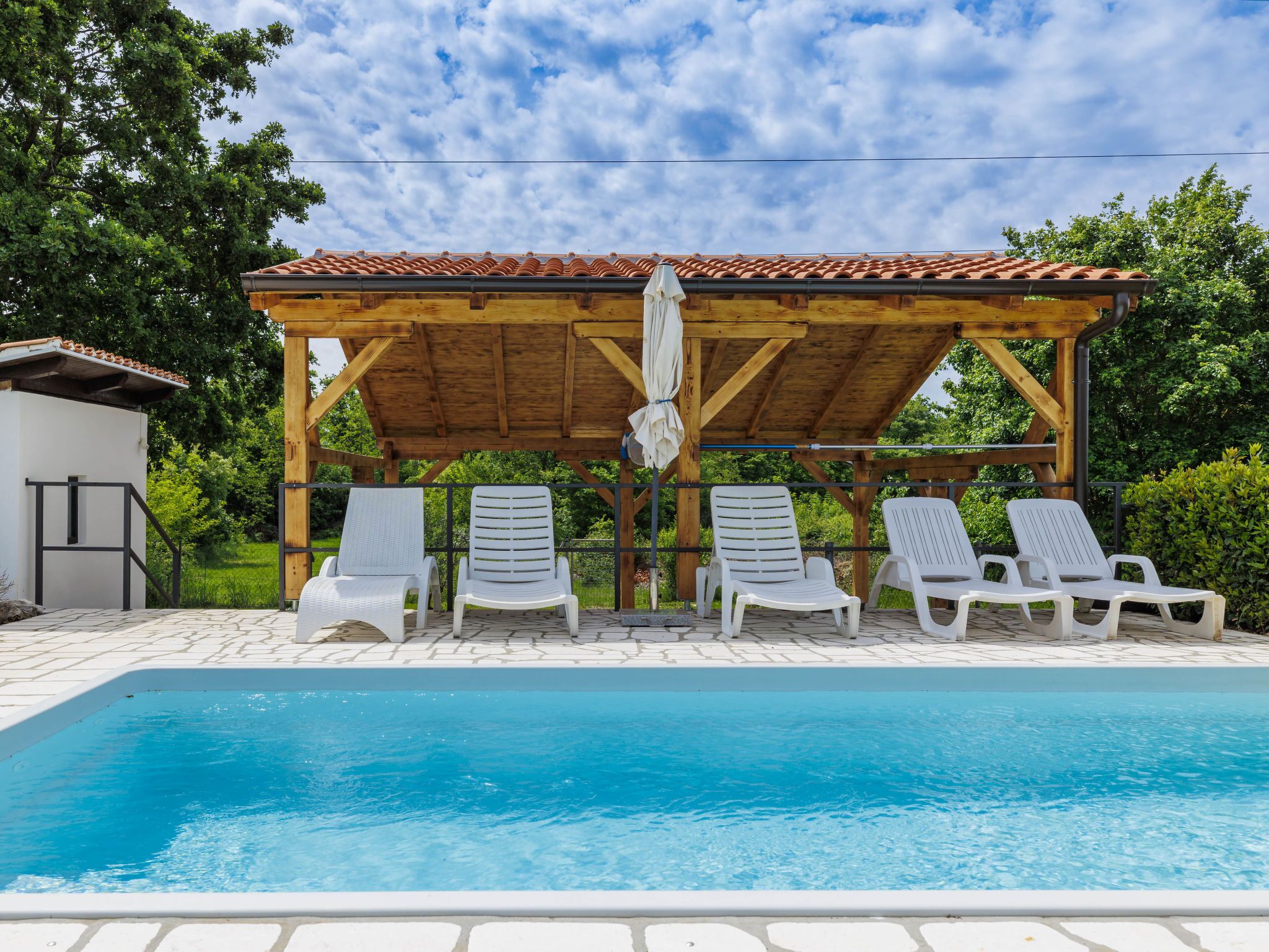 A pool area with a wooden pergola, white lounge chairs, and a clear blue pool.