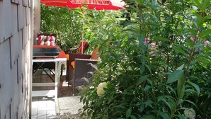 Un espace patio agrémenté d’un parasol rouge, de sièges d’extérieur et d’un jardin où poussent différentes espèces de plantes.