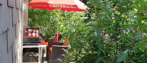 A patio area with a red umbrella, outdoor seating, and a garden with various plants.