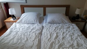 Un lit double avec une literie blanche, deux tables de chevet avec des lampes et une petite table de nuit avec un téléphone et une lampe.