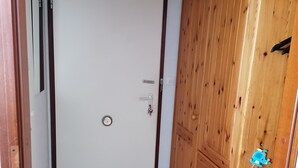 Une pièce avec une armoire en bois, une porte blanche dotée d’un trou de serrure, un tapis rouge et un objet bleu sur le sol.