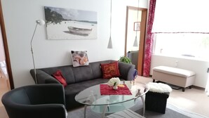 Un salon moderne avec une table basse en verre, un canapé gris et un coussin rouge.
