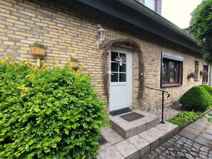 A brick house with a white door, a small porch, and a window with a flower box.